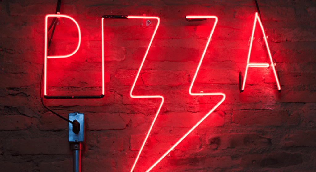 Neon pizza sign against a brick wall.