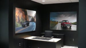 An office with black walls featuring two large photos of cars on scenic roads, one desk, and a swivel chair.