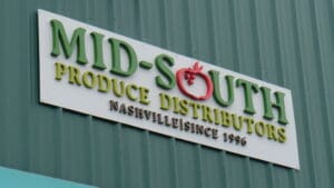 A sign on a green wall reads "mid-south produce distributors nashville since 1996," with a red tomato as the dot of the letter "i" in "mid.