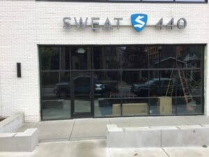 Front view of "sweat 440" fitness studio, displaying large glass windows and entrance, with signage above, on an urban street.