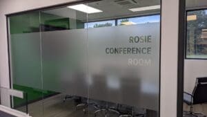 Glass door labeled "rosie conference room" leading to an office meeting room with chairs visible through frosted glass.