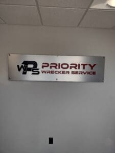 A sign reading "wps priority wrecker service" displayed on a wall, featuring red and black text on a white background.
