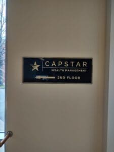 Sign that reads "capstar wealth management 2nd floor" mounted on a wall beside a stairwell, featuring a logo with a star.