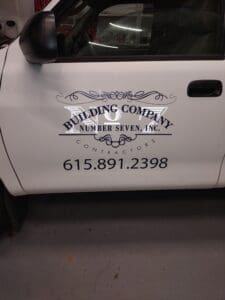 White truck door with a logo and text that reads "building company number seven, inc., contractors", along with a phone number.