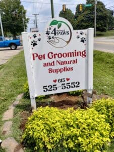 Roadside advertisement for '4 the love of paws' featuring pet grooming and natural supplies services, with contact number displayed, set against a street background.