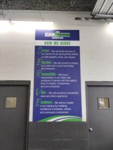 Vertical banner in a garage showcasing "the car care center" values such as service, compassion, responsibility, and excellence, displayed in white and blue text on a green background.