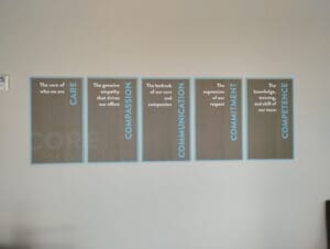 Four decorative panels on a wall displaying values: care, compassion, communication, commitment, each with an accompanying descriptive sentence.