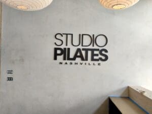 Wall with the logo 'studio pilates nashville' displayed in bold, black letters, accompanied by unique round lighting fixtures above.