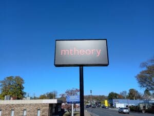 A billboard displaying the word "mtheory" in lowercase letters, set against a clear blue sky.