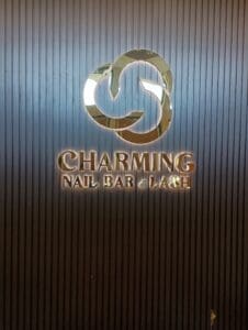 Illuminated sign of "charming nail bar & lash" on a ribbed dark background with a circular logo above the text.