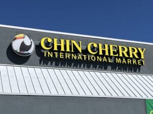Storefront sign for "chin cherry international market" featuring a colorful logo with a puffin bird on a blue sunny sky background.