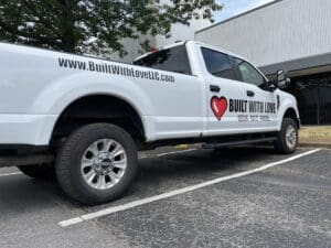 A white pickup truck with "builtwithlovellc.com" branding and a heart logo parked outside a building.