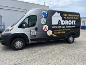 A parked van featuring advertising decals for adroit restoration & remediation, including logos, a qr code, and contact information.