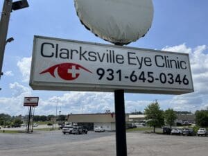 Sign for "clarksville eye clinic" with contact number and a logo, displayed outdoors under a partly cloudy sky.