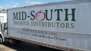 Side view of a white delivery truck with "mid-south produce distributors" and contact information on it, parked under a clear sky.