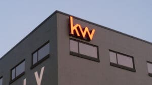 Neon "kw" sign atop a modern gray building against a dusk sky.