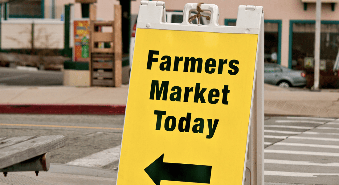 A yellow sign reads "Farmers Market Today" with an arrow pointing left. The sign is placed on a sidewalk in an urban area.