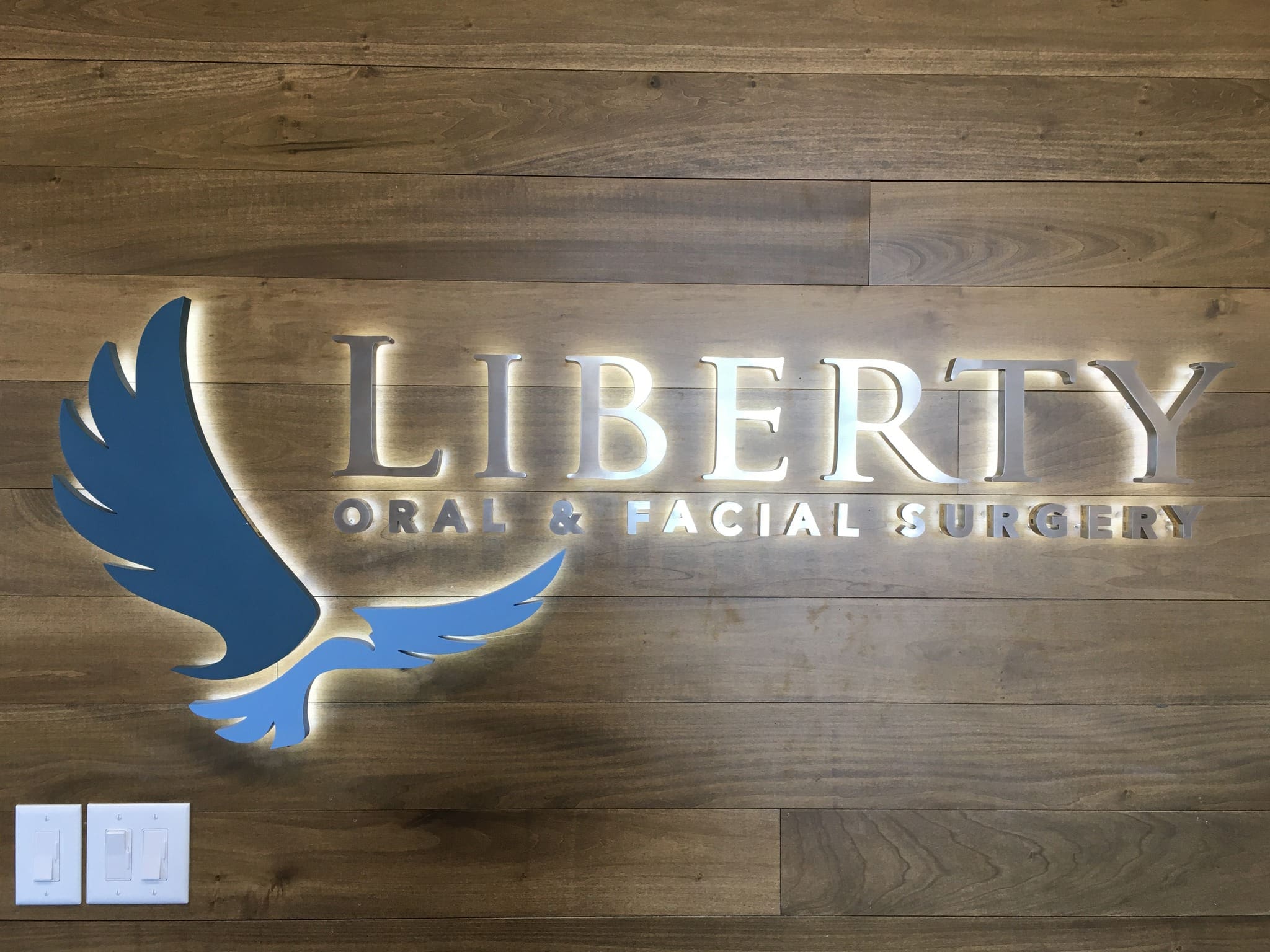 A wall sign with a blue eagle silhouette and the words "Liberty Oral & Facial Surgery" on a wood background.