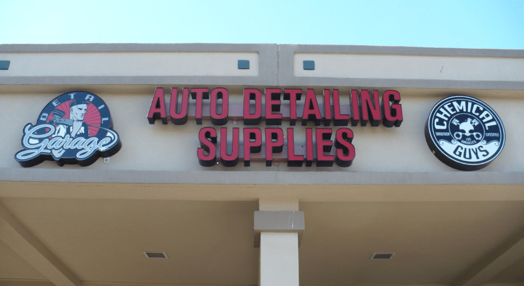 Exterior sign for an auto detailing supplies store, featuring logos for Detail Garage and Chemical Guys, mounted on a beige building. Cost to install business signs