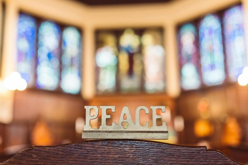 Church Sign in Nashville Wooden "Peace" sign on a pew with blurred stained glass windows in the background.