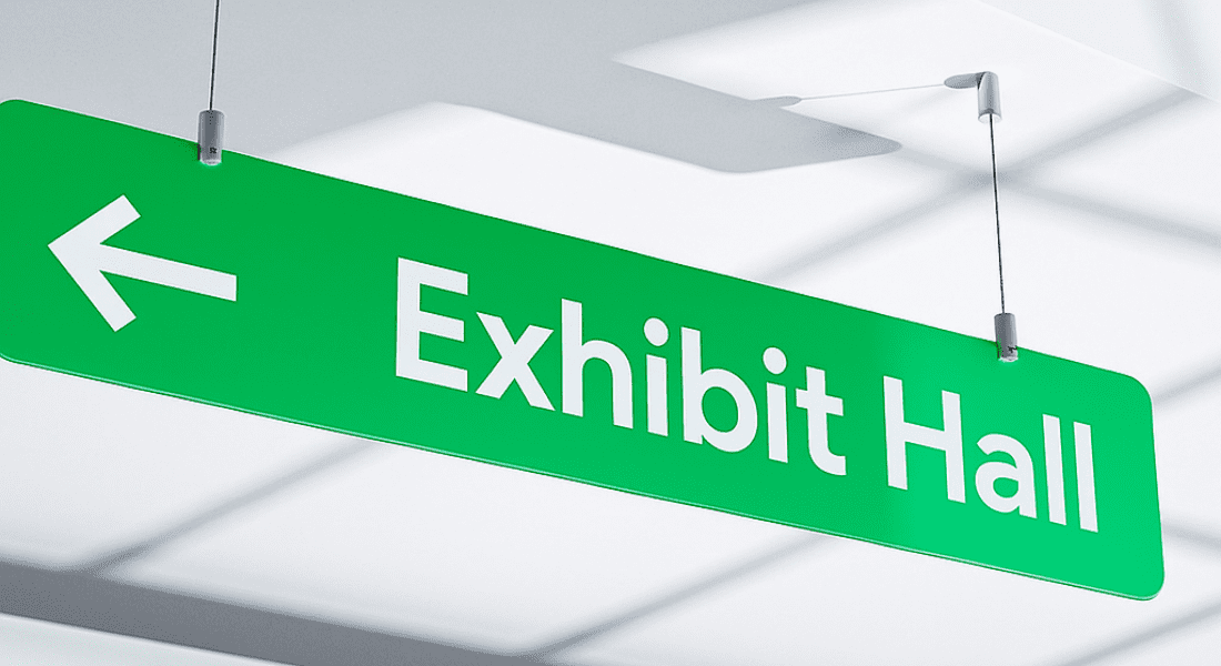 Green sign with white text reading "Exhibit Hall" and a left-pointing arrow, hanging from the ceiling.