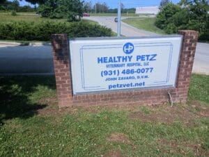 A brick sign reads "Healthy Petz Veterinary Hospital, LLC, (931) 486-0077, John Zavaro, D.V.M., petzvet.net" beside a road and grassy area.
