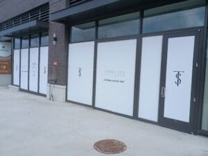 Storefront with windows covered in white signage displaying "Ioska Spa" and "Opening August 2025" along with a logo and no visible activity inside.