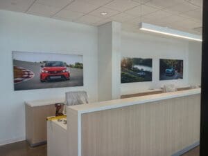 Reception area with light wood desk, tool on counter, and three framed car photographs on the wall behind.
