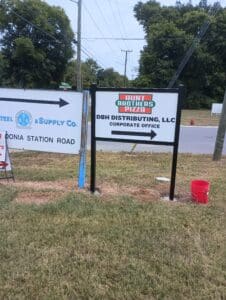 A sign for Hunt Brothers Pizza and DBH Distributing, LLC Corporate Office stands on grass near a road, next to another business sign.