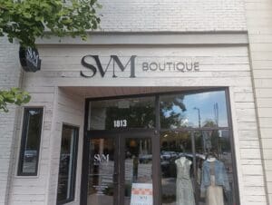 Storefront of SVM Boutique with large sign above the entrance, glass door, window displays, and mannequins dressed in light-colored clothing. Address 1813 is above the door.