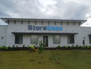A white commercial building with the sign "StoreEase" above the entrance; two workers are tending to landscaping in front.
