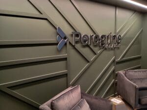 A modern waiting area with grey chairs and a green wall displaying the "Peregrine Health" logo in raised letters.