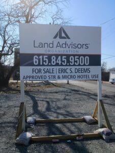 A large outdoor sign reads: "Land Advisors Organization. 615.845.9500. For Sale | Eric S. Deems. Approved STR & Micro Hotel Use." The sign stands on gravel, supported by sandbags.