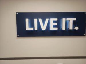 A blue sign with large white letters on a wall displays the phrase "LIVE IT.