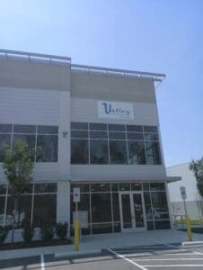 A modern office building with a sign reading "Valley" above the entrance, accessible parking spaces, and large windows on the ground floor.