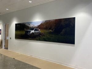 A large wall-mounted photograph shows an SUV parked on grass in a scenic mountain landscape with trees and distant snowy peaks.