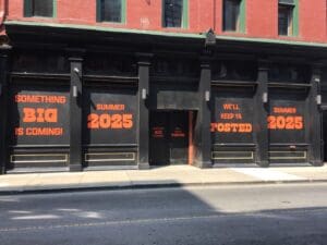 Storefront with blacked-out windows displays bold orange text: "Something big is coming! Summer 2025. We'll keep ya posted. Summer 2025.