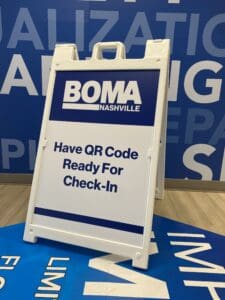 A white sandwich board sign reads "BOMA Nashville. Have QR Code Ready For Check-In" against a blue background with large partial text.