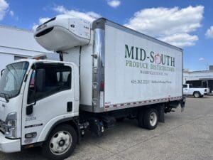A refrigerated delivery truck with "Mid-South Produce Distributors" branding is parked outside under a blue sky with scattered clouds.