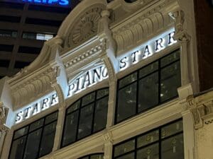 A building facade at night displays illuminated letters spelling "STARR PIANO" above large windows.