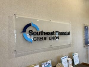 Wall-mounted sign reading "Southeast Financial Credit Union" with a blue and black logo, displayed above brochures and informational materials.