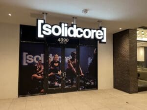 Exterior of a [solidcore] fitness studio at 4090 Ste 103, with photos of people exercising displayed on the glass doors.