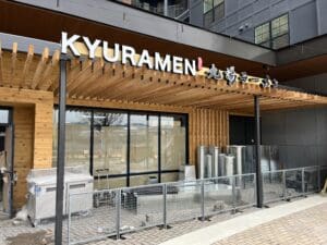Exterior of a Kyuramen restaurant under construction, with building materials and equipment visible outside, and the restaurant sign displayed above the entrance.