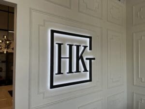 A black and white illuminated sign with the letters "HKG" is mounted on a white paneled wall in an interior space.