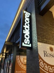 Illuminated [solidcore] sign mounted on a brick wall outside a commercial building at dusk.