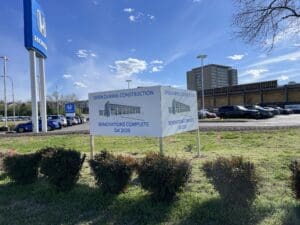 A sign in front of a Honda dealership reads "Open During Construction. Renovations Complete Q4 2025" with an illustration of the future building. Cars and buildings are visible in the background.