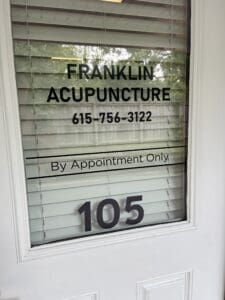 Glass door with sign reading "Franklin Acupuncture, 615-756-3122, By Appointment Only" and the number 105, with closed blinds and a fence visible outside.