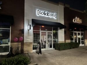 Exterior of [solidcore] fitness studio at night, with illuminated sign, glass doors, sidewalk, and pink balloons by the entrance.