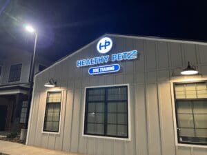 A building at night with a lit sign reading "Healthy Petz Dog Training" above three windows on the exterior.