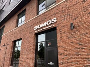 Exterior view of a brick building with large windows and a sign that reads "SOMOS PILATES NASHVILLE" above the entrance.